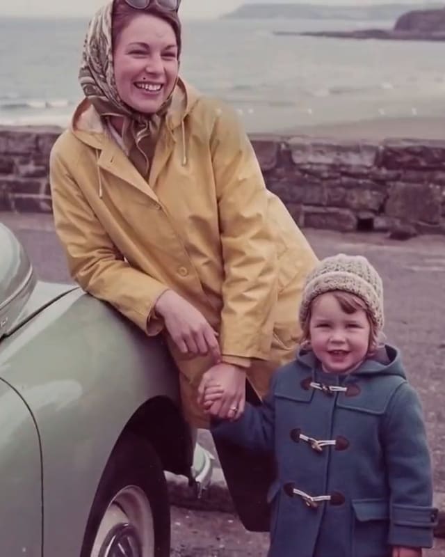 Eine junge Mutter im gelben Regenmantel lehnt am Meer an einem Auto und hält ihren kleinen Sohn an der Hand. Ein Bild aus unserem Beispielfilm; die Personen sind erfunden.